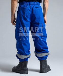 กางเกงยูนิฟอร์มทำงานขายาวสีน้ำเงินสด มุมด้านหลังเห็นเอวยางยืดด้านหลังพร้อมหูเข็มขัด กระเป๋าหลังทรงเรียบ และกระเป๋าคาร์โก้ด้านข้างฝาปิด ช่วงปลายขามีแถบสะท้อนแสงสีเงินคาดรอบขาทั้งสองข้าง พร้อมปลายขาจั๊มยาง ใส่รองเท้านิรภัยสีดำ ฉากสตูดิโอพื้นเทา