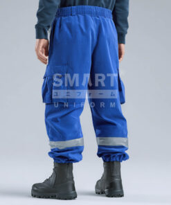 กางเกงยูนิฟอร์มทำงานขายาวสีน้ำเงิน มุมด้านหลังเห็นเอวยางยืดและทรงเรียบ กระเป๋าหลังแบบเรียบพร้อมกระเป๋าคาร์โก้ด้านข้างทั้งสองข้าง ช่วงปลายขามีแถบสะท้อนแสงสีเงินคาดรอบขาทั้งสองข้าง ปลายขาจั๊ม ใส่รองเท้านิรภัยสีดำ ฉากสตูดิโอพื้นสีอ่อน