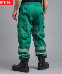 กางเกงยูนิฟอร์มทำงานขายาวสีเขียวมรกต มุมด้านหลังเห็นขอบเอวด้านหลังแบบยางยืดและหูเข็มขัด กระเป๋าคาร์โก้ด้านข้างฝาปิดทั้งสองข้าง ช่วงปลายขามีแถบสะท้อนแสงสีเงินคาดรอบขาทั้งสองข้าง ใส่รองเท้านิรภัยสีดำ ฉากสตูดิโอพื้นเทา