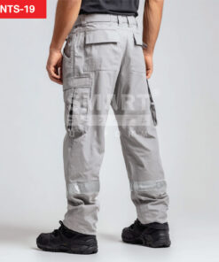 กางเกงยูนิฟอร์มทำงานขายาวสีเทาอ่อน มุมด้านหลังเห็นหูเข็มขัด กระเป๋าหลังทรงเหลี่ยมแบบมีฝาปิด และกระเป๋าคาร์โก้ด้านข้างฝาปิด ช่วงปลายขามีแถบสะท้อนแสงสีเงินคาดรอบขาทั้งสองข้าง ใส่รองเท้านิรภัยสีดำ ฉากสตูดิโอพื้นขาว