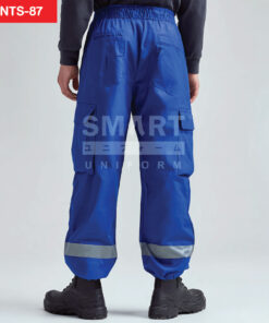 มุมหลัง กางเกงช็อปช่าง สีน้ำเงินสด เอวยางยืด กระเป๋าหลังคู่ แถบสะท้อนแสง รอบขา ยืนถ่ายสตูดิโอ เงานุ่ม ใส่รองเท้านิรภัย